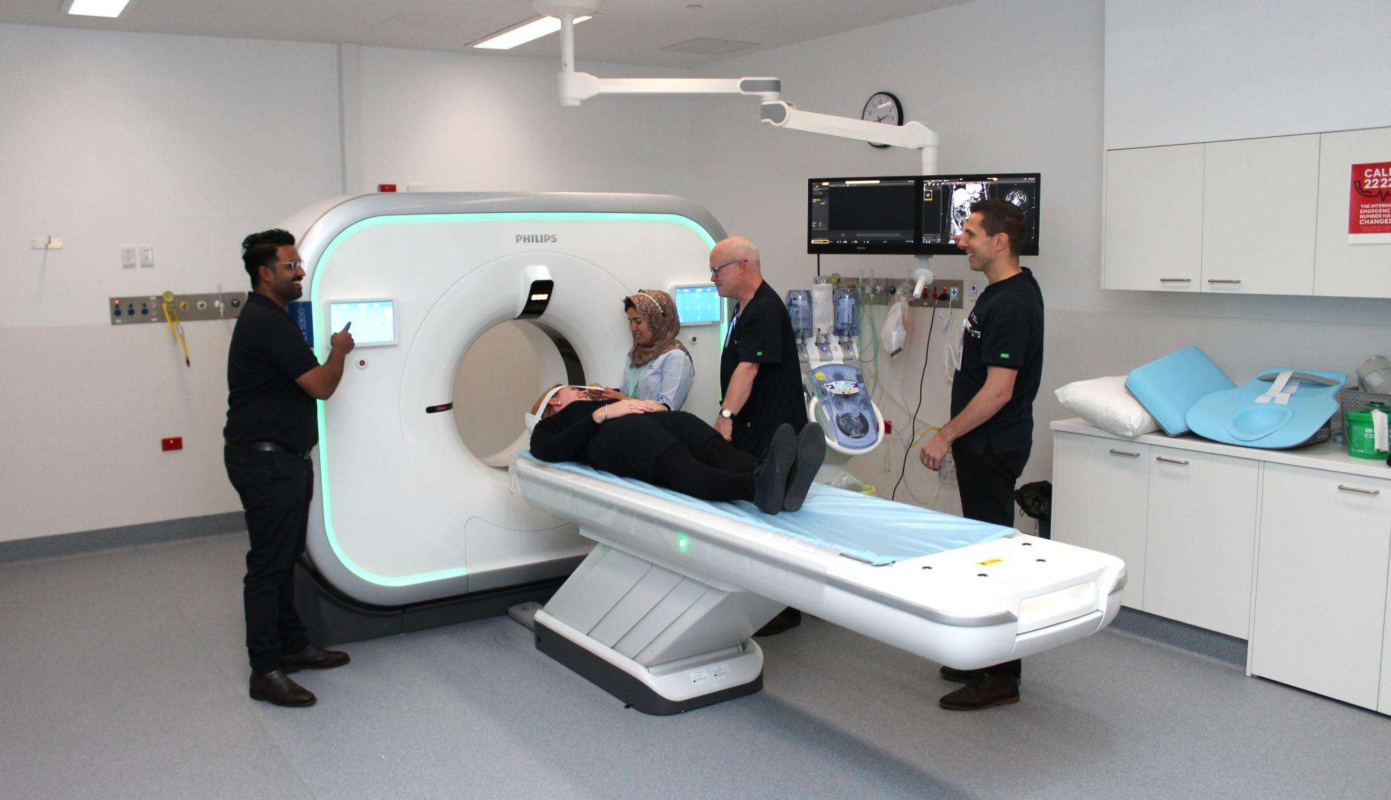 Patient laying down on a CT bed with staff preparing them for a CT scan.