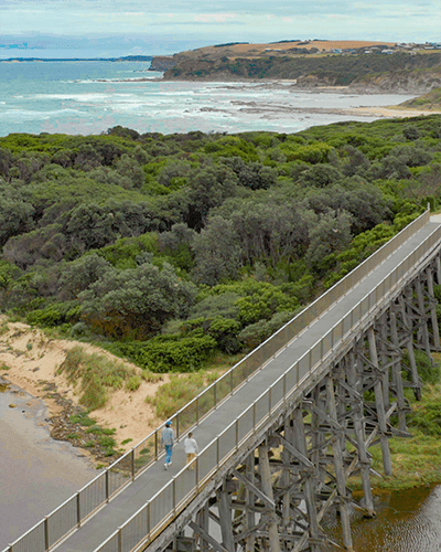 Two people walk across the rail bridge in Kilcunda